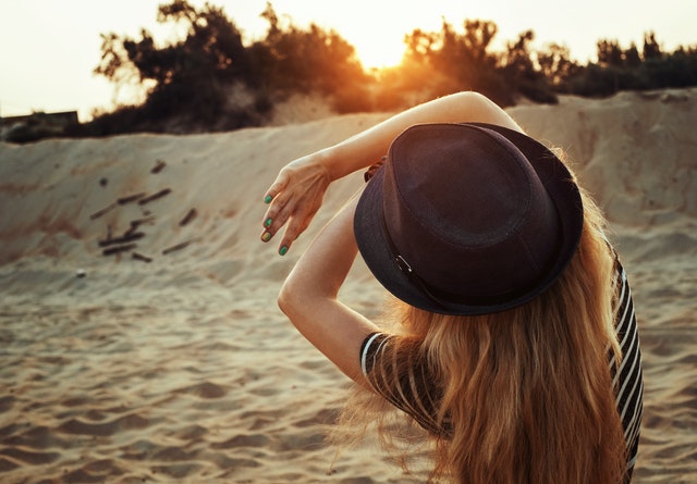 Žena v pásikovom tričku a s klobúkom na hlave stojí na pieskovej pláži.jpg